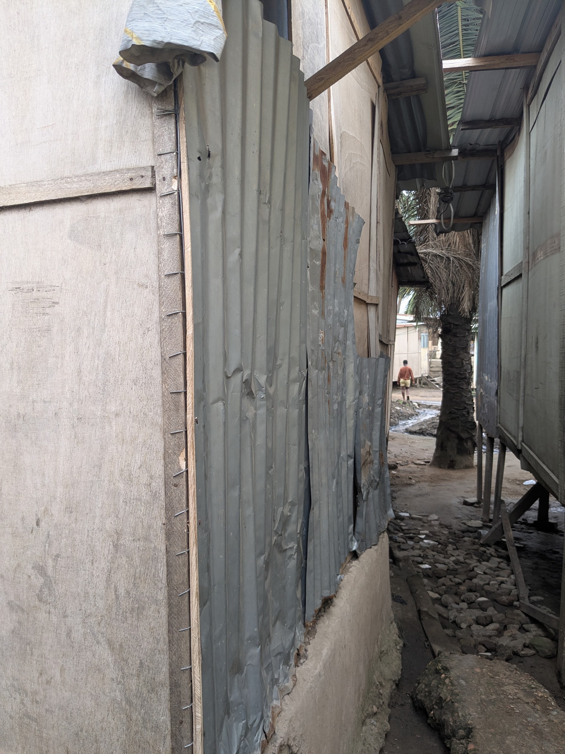 Narrow passage between homes, showing shared roof overhangs and open drainage channels