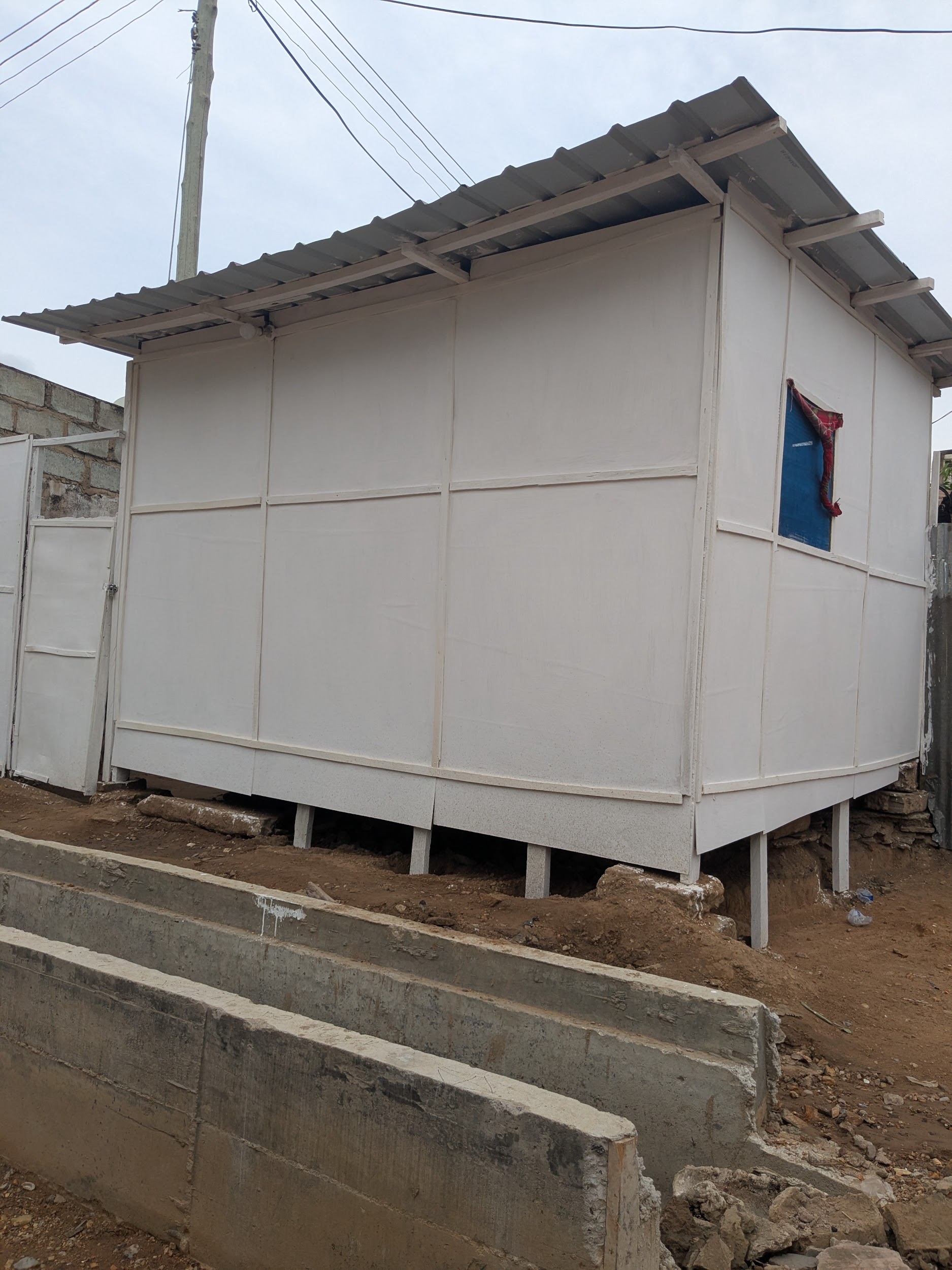 A newer fibre-cement panel structure in Agbogbloshie, raised on concrete columns with a corrugated metal roof